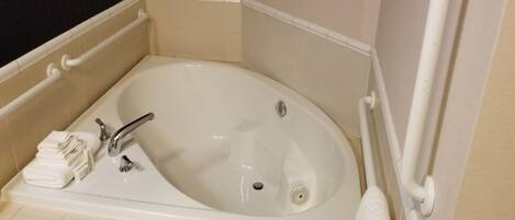 Eine Eckbadewanne mit integriertem Waschbecken, einer Handstange und einem Handtuchhalter.