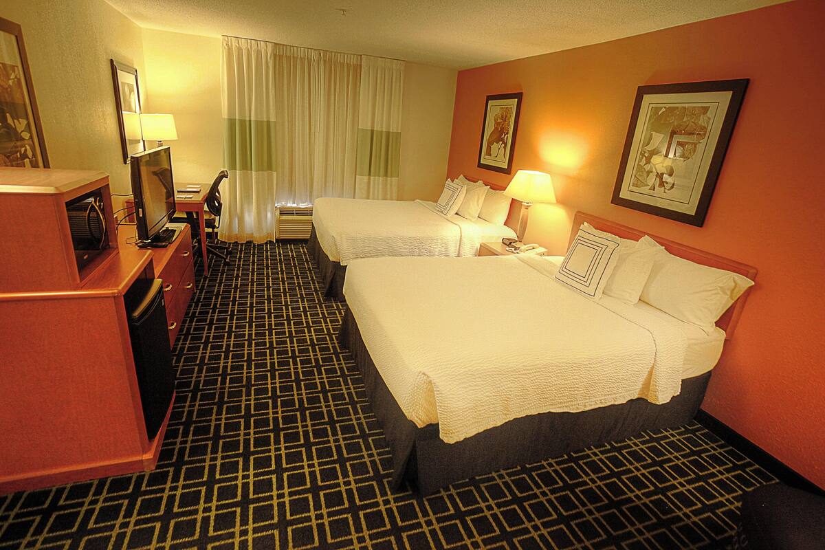Ein Hotelzimmer mit zwei Betten, einem Schreibtisch mit Computer, einem Fernseher und einem Badezimmer.