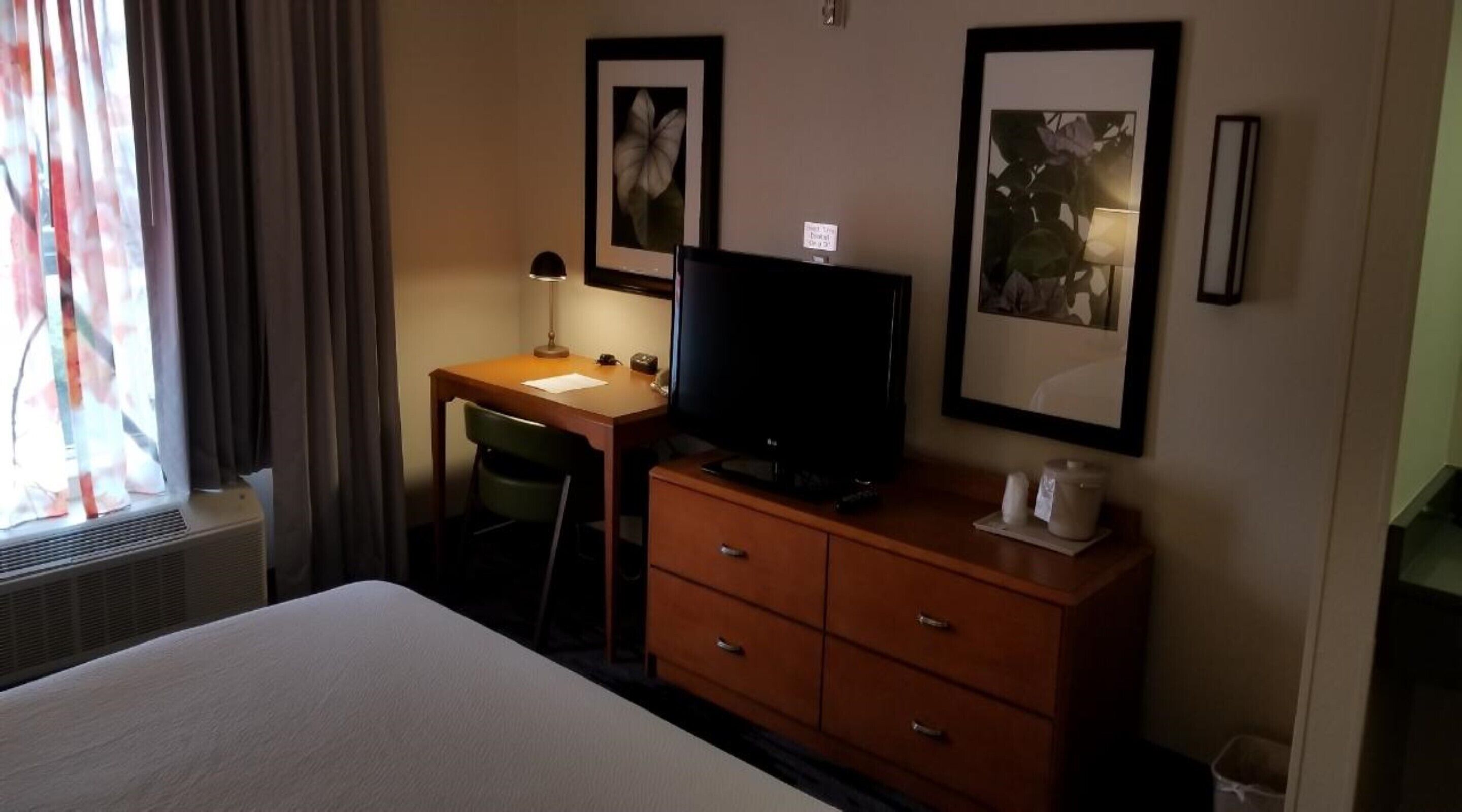 Une chambre d’hôtel avec un lit, un bureau équipé d’un ordinateur, une télévision et deux tableaux encadrés accrochés au mur.