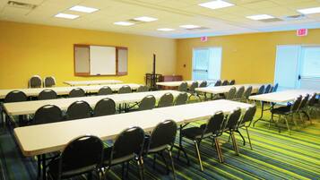 A conference room with multiple tables and chairs, a whiteboard, and windows with blinds.