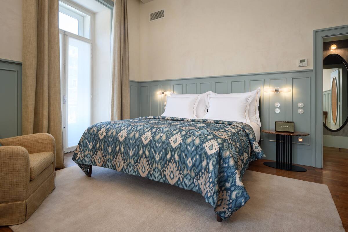 Un dormitorio con cama, una silla, una mesita de noche y un espejo.