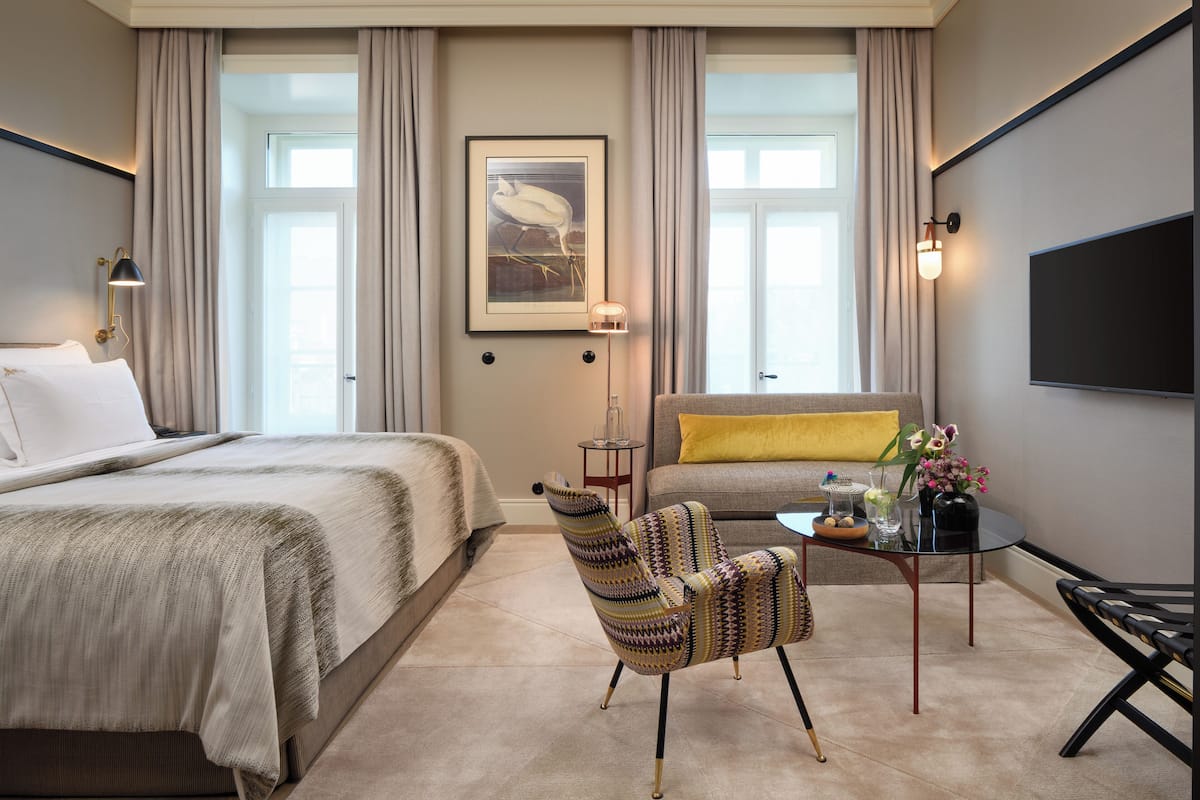 Una habitación de hotel con una cama grande, un sofá, una mesita con un florero y una silla.