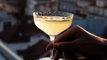 Un verre à cocktail posé sur la rambarde d’un balcon, avec une vue sur la ville et l’eau en arrière-plan.