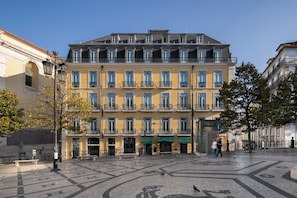 Un immeuble à plusieurs étages, doté d’une façade jaune, de nombreux balcons et d’un trottoir pavé devant l’entrée.