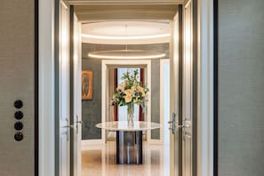 Un pasillo con una mesa redonda y un jarrón de flores, que conduce a una habitación con un ventanal grande y un cuadro en la pared.