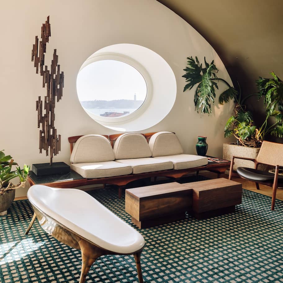 A modern interior with a curved ceiling, a round skylight, a sofa with cushions, a wooden coffee table, a small side table, and a potted plant.