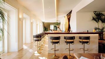 Een moderne bar met een lange toonbank, verschillende barstoelen en een potplant.