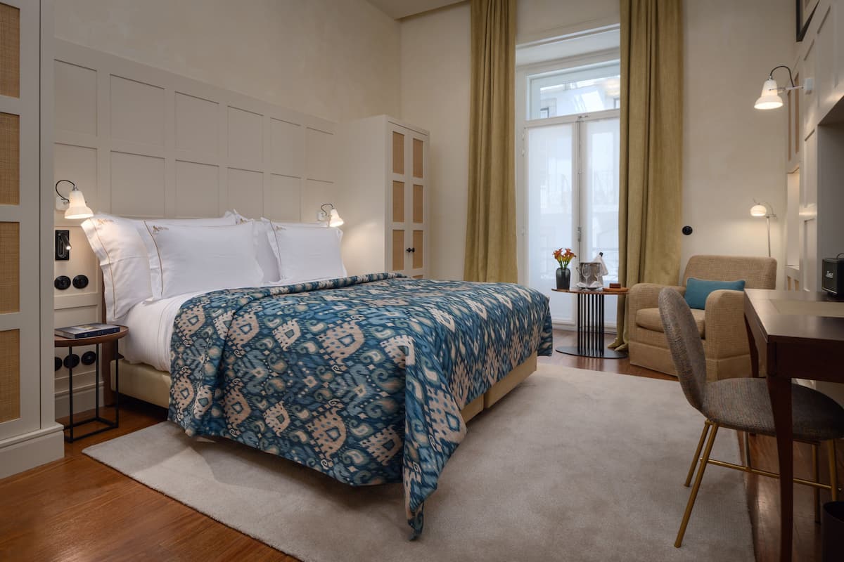 Una habitación de hotel con cama, escritorio, silla y ventana con cortinas.