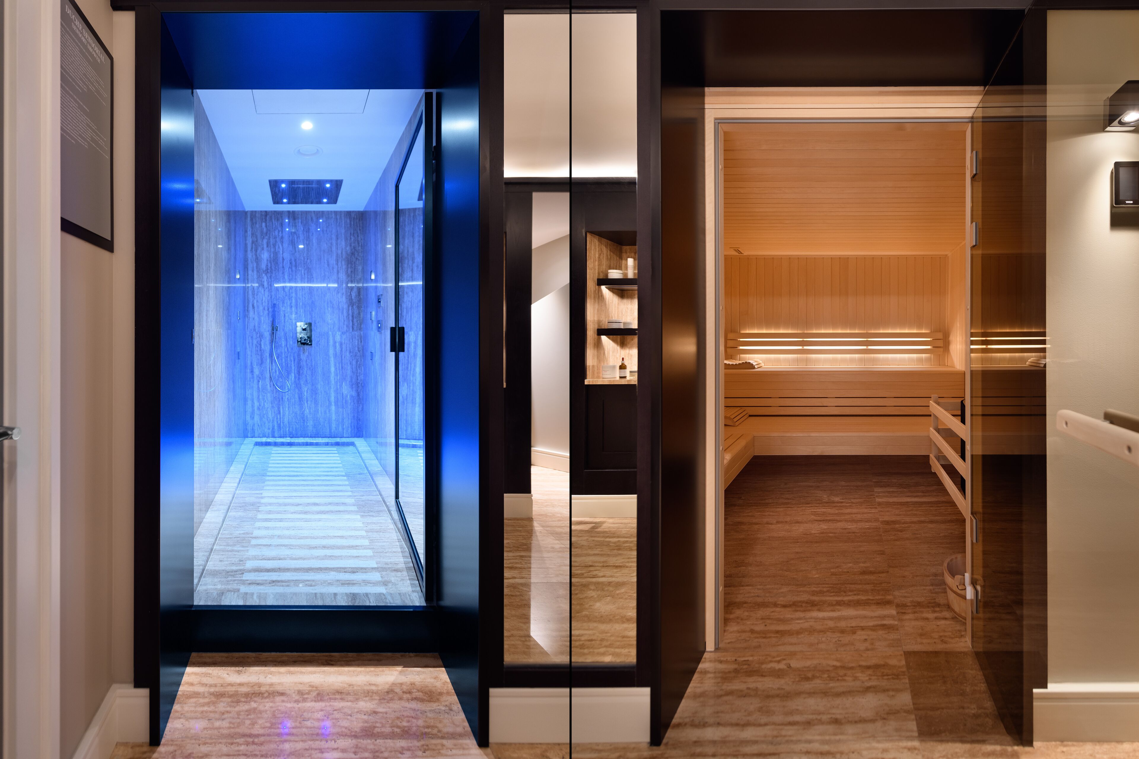 A modern hotel lobby with a glass elevator, wooden flooring, and a reception area with a wooden reception desk.