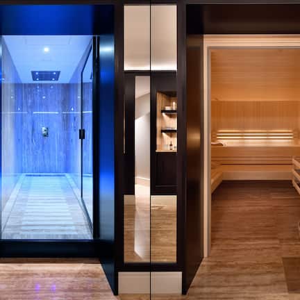 A modern hotel lobby with a glass elevator, wooden flooring, and a reception area with a wooden reception desk.