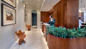 Un hall d’hôtel avec un comptoir d’accueil en bois, des œuvres d’art encadrées accrochées aux murs et un sol à motifs.