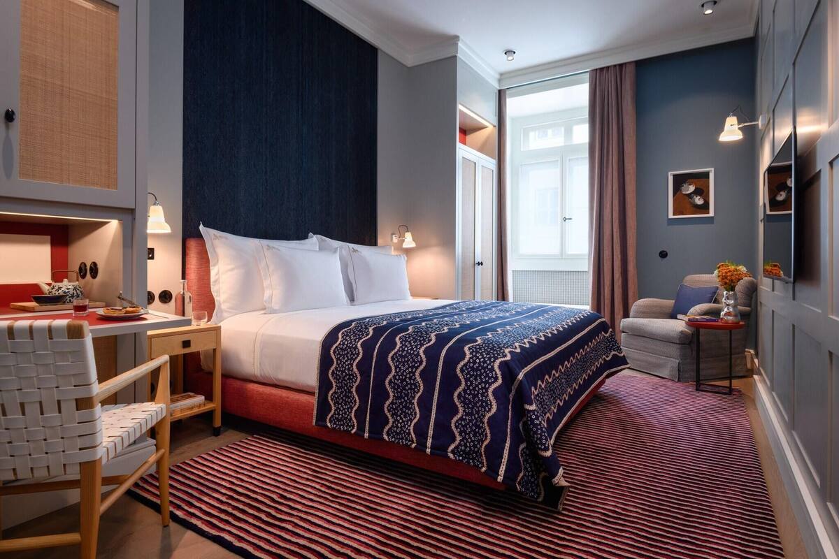 Ett hotellrum med en säng, ett nattduksbord, en stol och utsikt över omgivningarna.