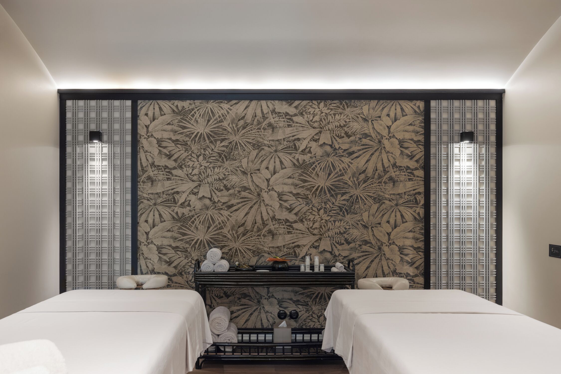 A hotel room with two beds, a large floral-patterned wall, a small table with toiletries, and a nightstand.