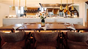 Un restaurant moderne avec une longue table à manger, de nombreuses chaises et une cuisine en arrière-plan.