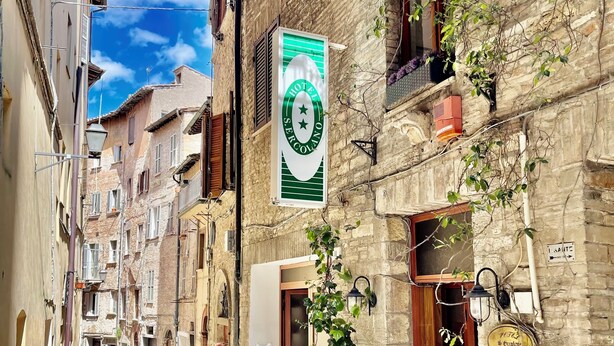 A narrow street with stone buildings, a visible hotel sign, and potted plants on the ground floor. - Hotel Sant'Ercolano (Perugia)