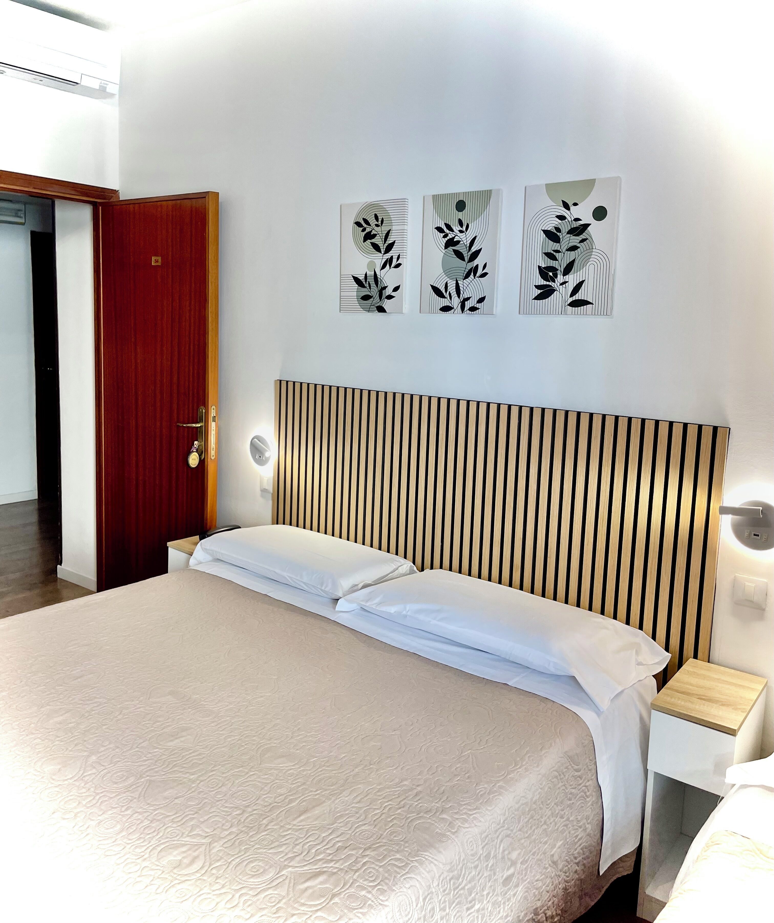 A hotel room with a bed, wooden headboard, bedside tables, and wall art.
