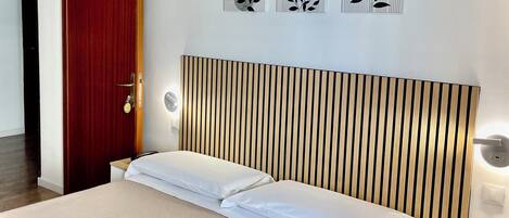 A hotel room with a bed, wooden headboard, bedside tables, and wall art.