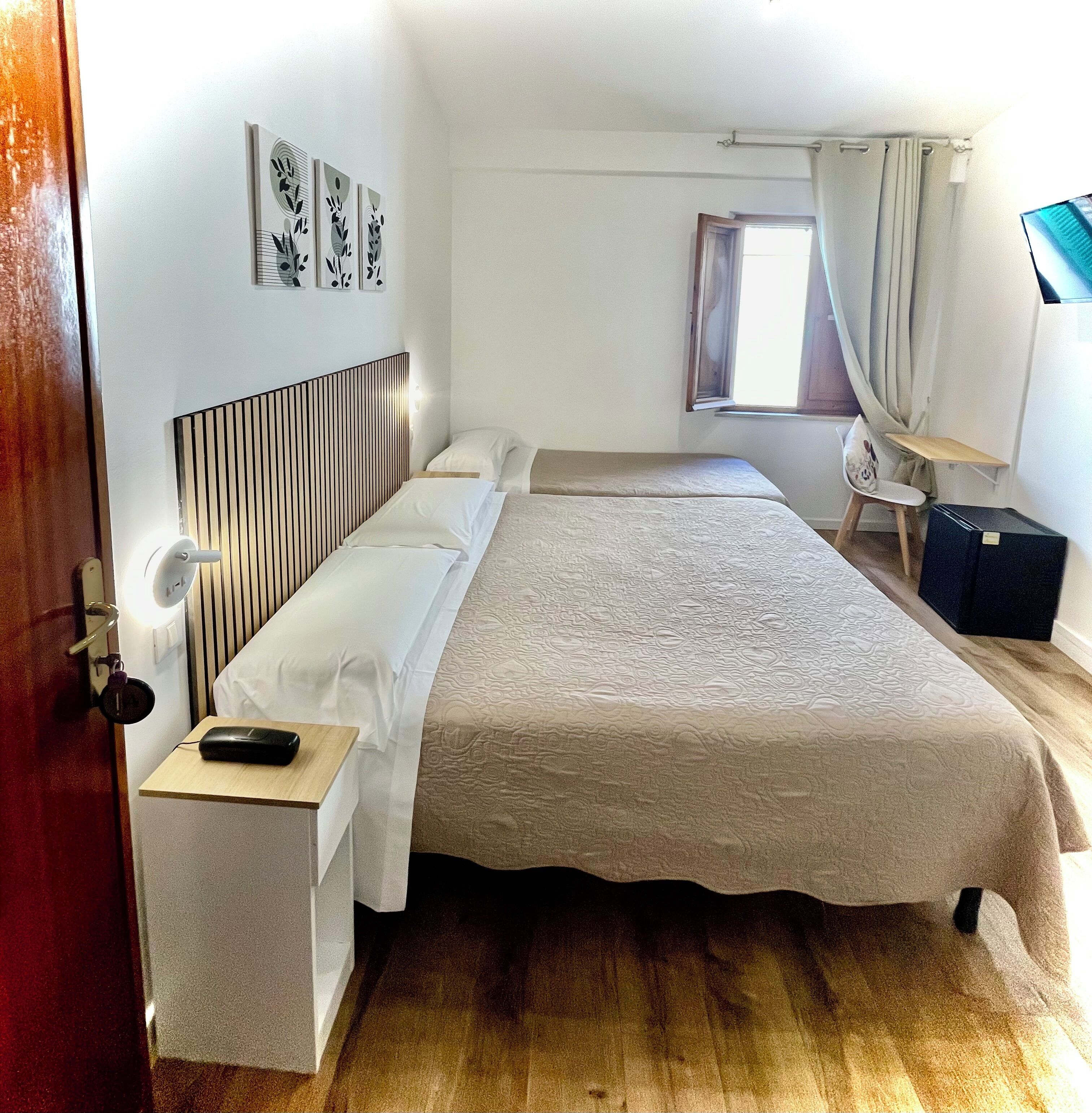 A bedroom with a bed, bedside table, lamp, and a window with curtains.