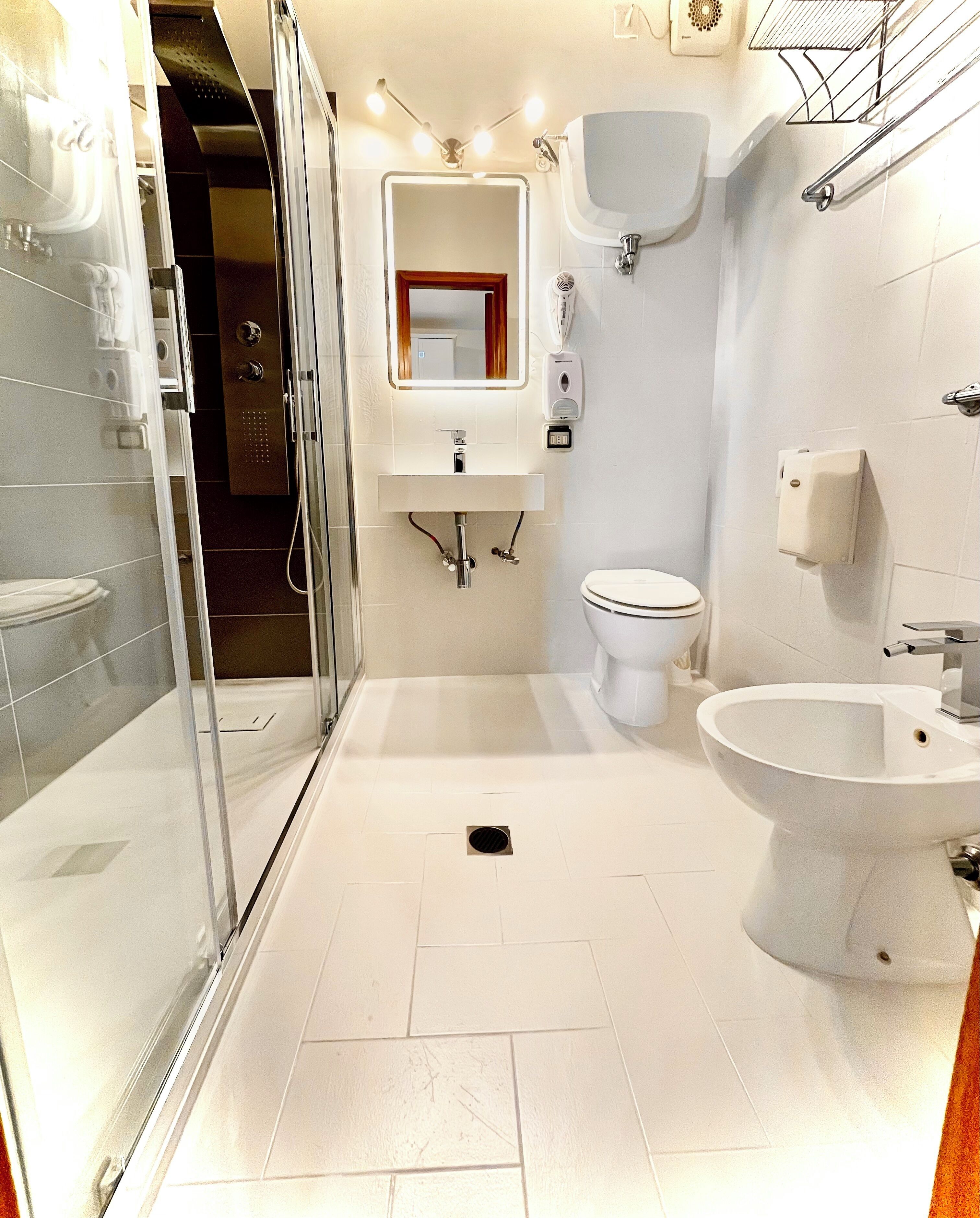 A modern bathroom with a glass shower enclosure, a pedestal sink, a toilet, and a bidet.