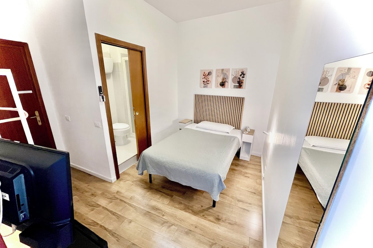 Une chambre d’hôtel de taille réduite, comprenant un lit, une table de chevet et un petit bureau avec une chaise.