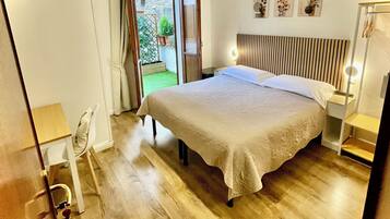 Ein Schlafzimmer mit einem großen Bett, Holzboden, einem kleinen Tisch, einem Stuhl und Blick auf einen Garten durch eine geöffnete Tür.
