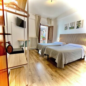 A hotel room with two beds, a wooden floor, a radiator, a television on the wall, and a window with curtains. - Hotel Sant'Ercolano (Perugia)