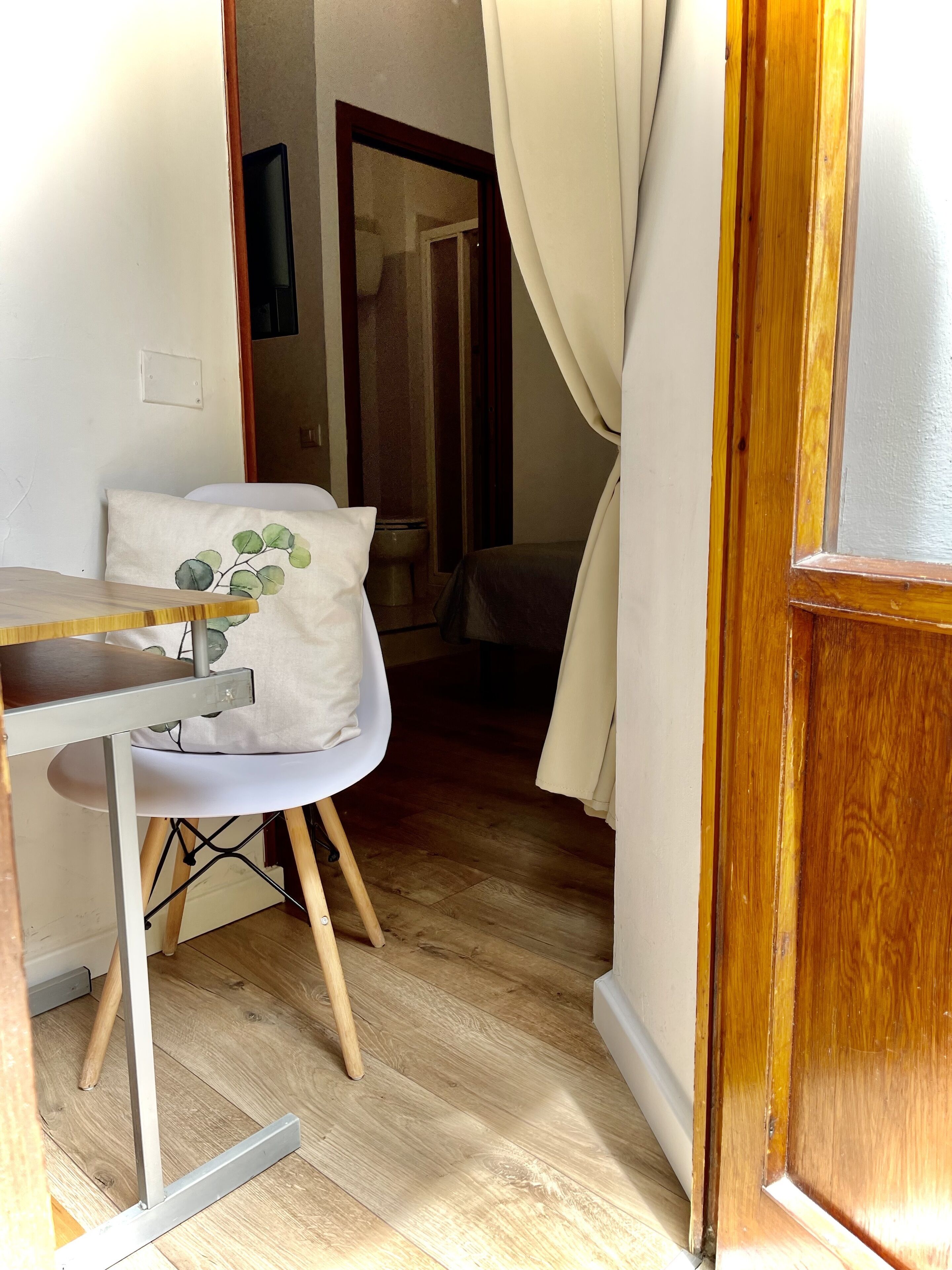 A room with a wooden floor, a white chair with a cushion, a small table, and a wooden door.
