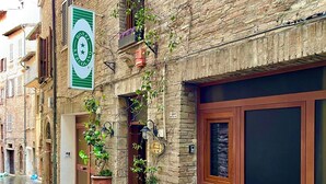 A historic building with a stone facade, a green sign indicating a hotel, and potted plants on the ground floor. - Hotel Sant'Ercolano (Perugia)