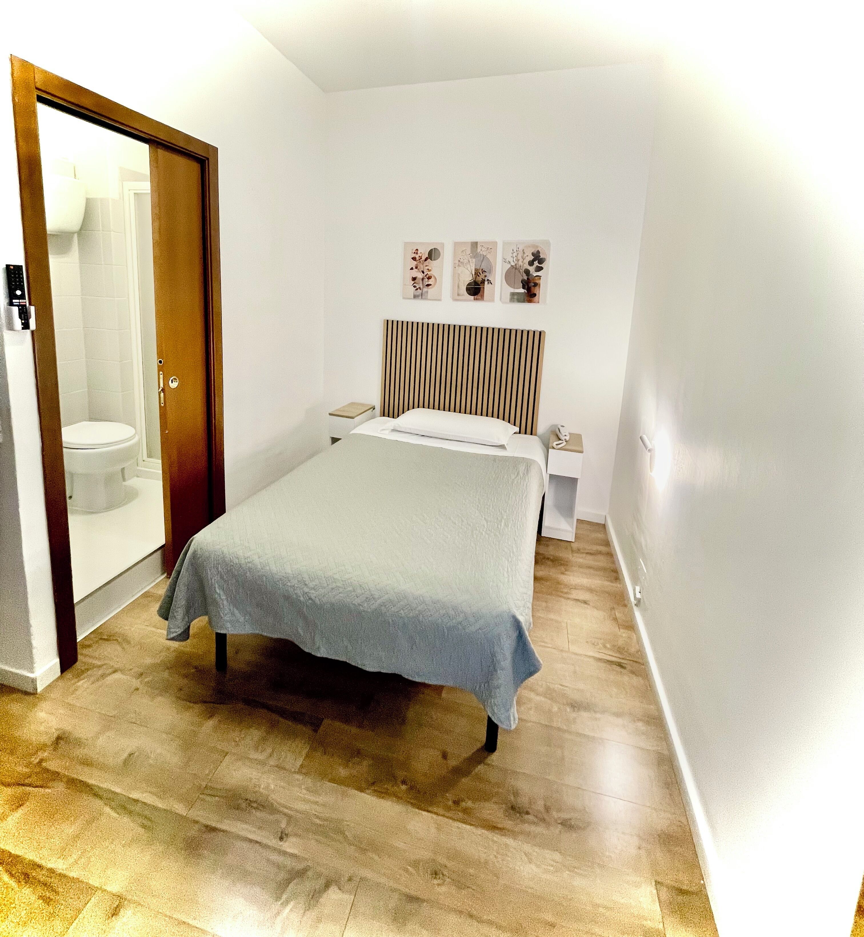 A bedroom with a bed, bedside tables, a nightstand, a wall-mounted phone, and a door leading to a bathroom.