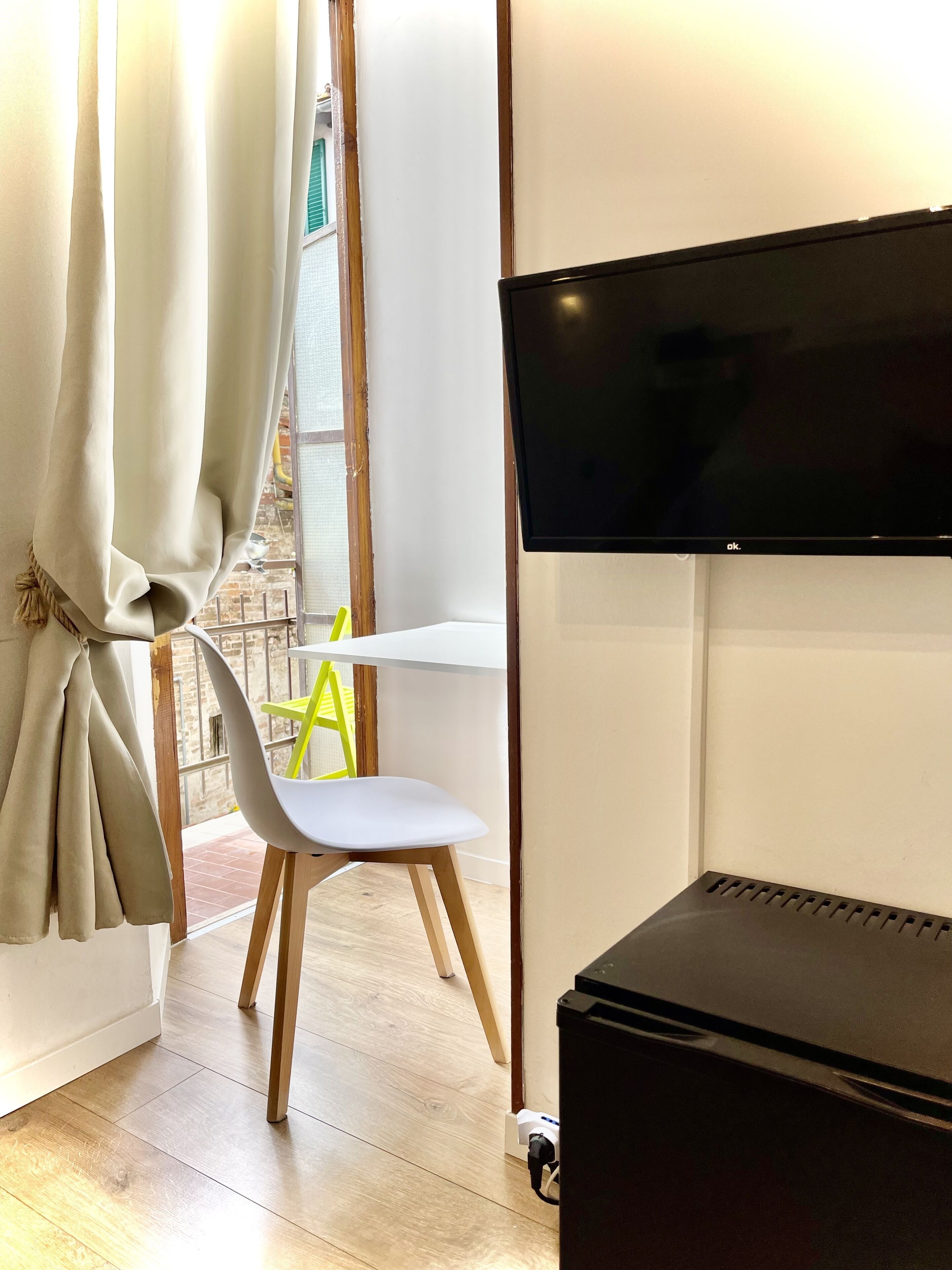 Una stanza con una TV a schermo piatto montata a parete, una sedia bianca e un pavimento in legno.