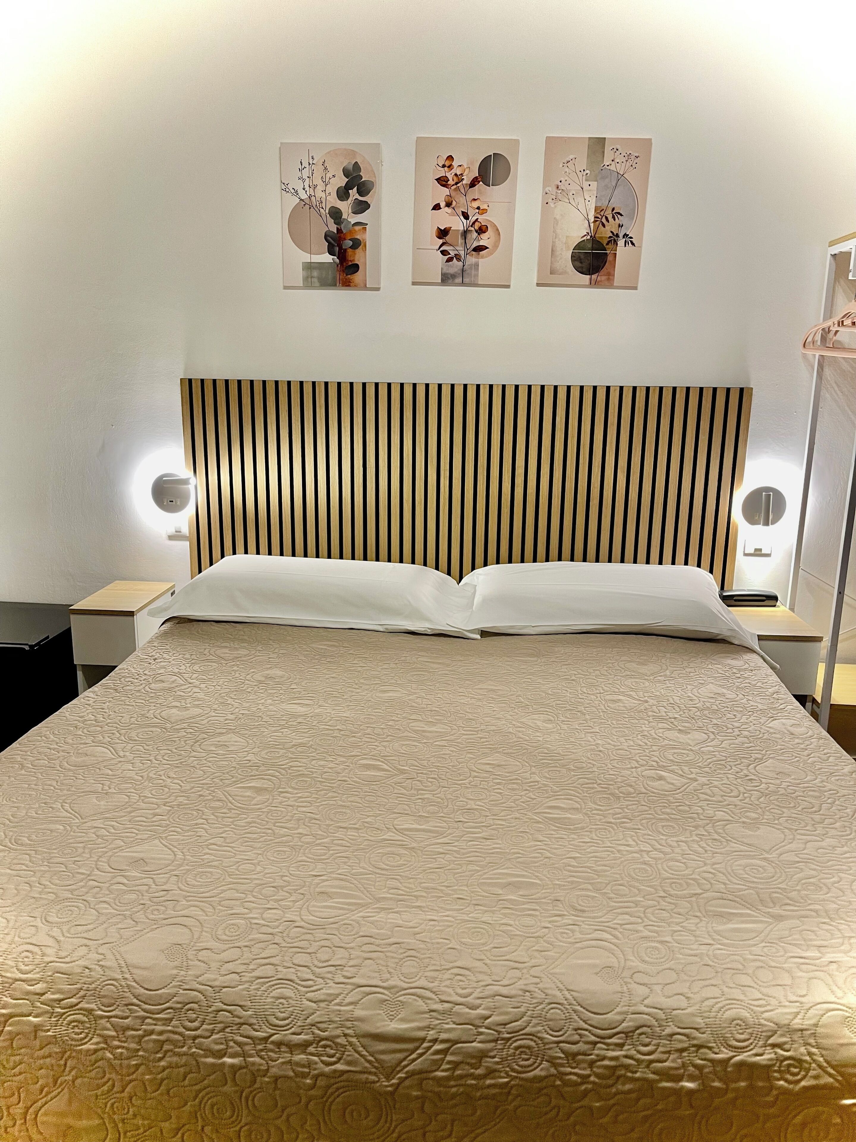 Habitación de hotel con una cama grande, cabecera de madera con listones y tres obras de arte colgadas en la pared que representan arreglos florales.