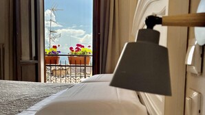 A hotel room with a bed, a bedside lamp, a window with curtains, and a view of the sky and flowers outside. - Hotel Sant'Ercolano (Perugia)