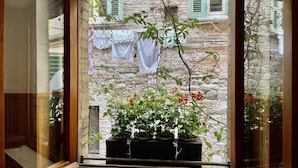 A window with a view of a stone building, a balcony with potted plants, and hanging laundry. - Hotel Sant'Ercolano (Perugia)