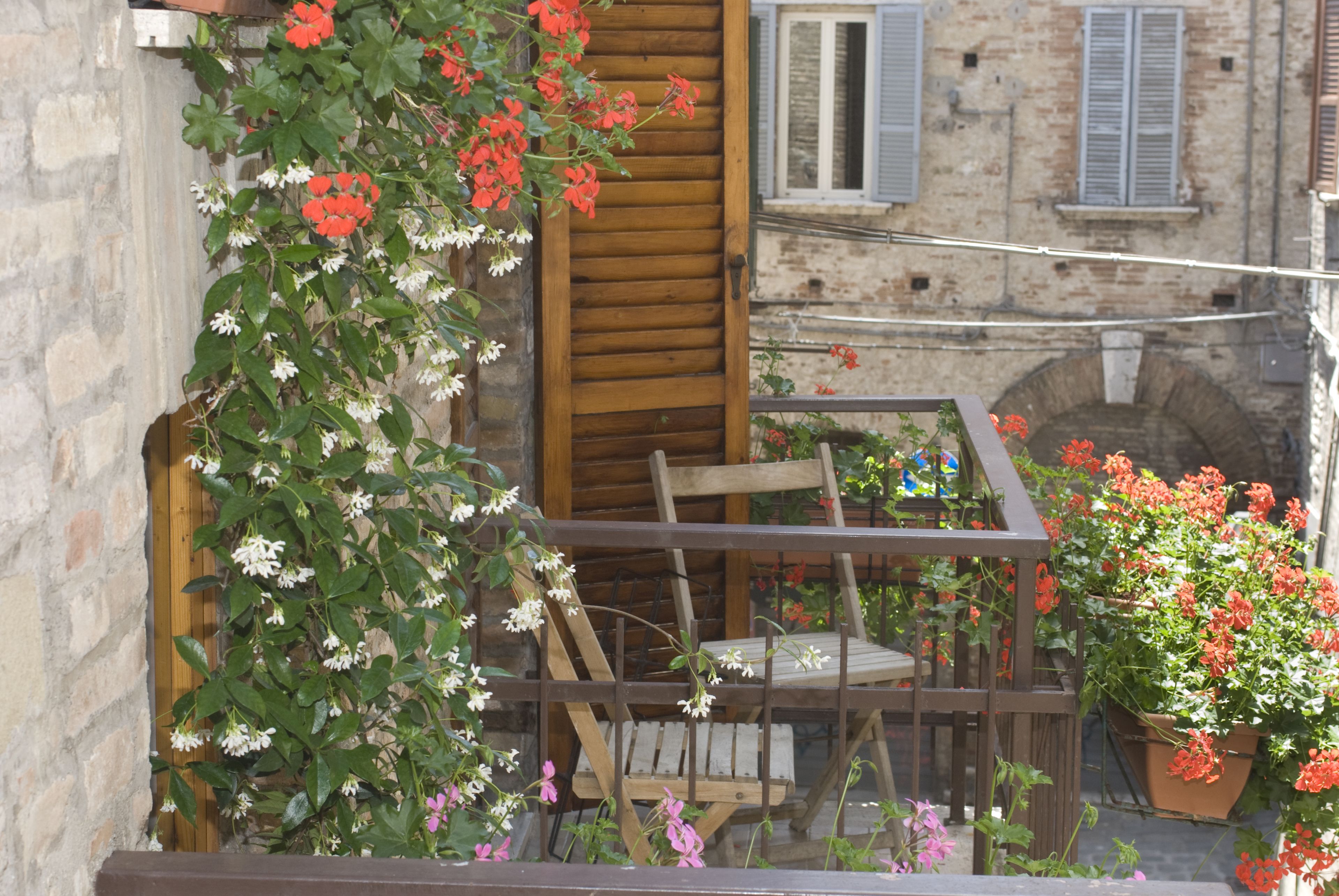 A balcony with a wooden chair and table, surrounded by potted plants and flowers.