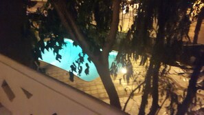 Vue d’une piscine la nuit, avec des arbres au premier plan.