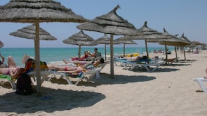 Uma praia com guarda-sóis de palha e espreguiçadeiras.