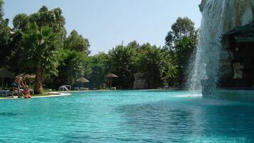 Relax by the serene pool surrounded by lush greenery and a soothing waterfall.
