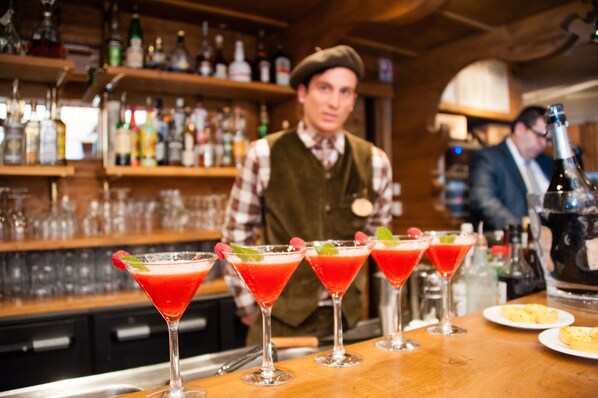 A bar with multiple red cocktails garnished with mint and strawberries, a bartender in uniform, and shelves stocked with various bottles. - Hotel Alpen Ruitor (Les Allues)