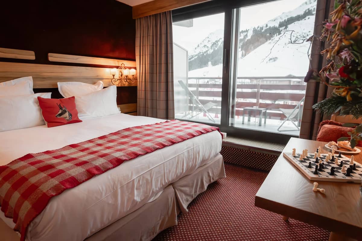Une chambre d’hôtel avec un grand lit, un jeu d’échecs et une vue sur une montagne enneigée.