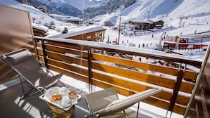 A balcony with a wooden railing overlooking a snowy mountain landscape, including ski slopes and buildings. - Hotel Alpen Ruitor (Les Allues)