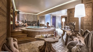 A spa area with a hot tub, wooden flooring, and a seating area with chairs and a table. - Hotel Alpen Ruitor (Les Allues)
