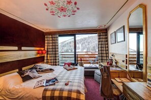 Habitación de hotel con cama, escritorio, silla, espejo grande y vista a una montaña nevada.