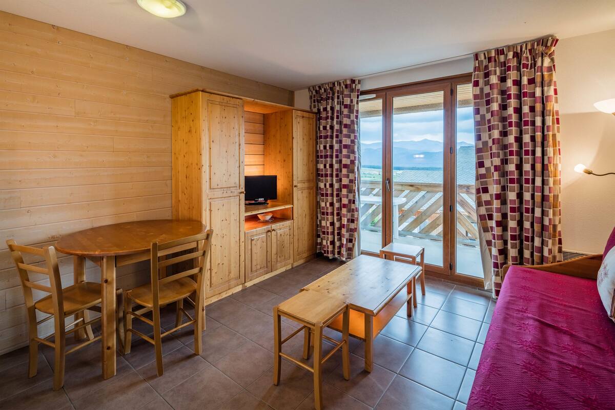 A wooden interior with a dining table, chairs, a bench, a TV, and a sofa.