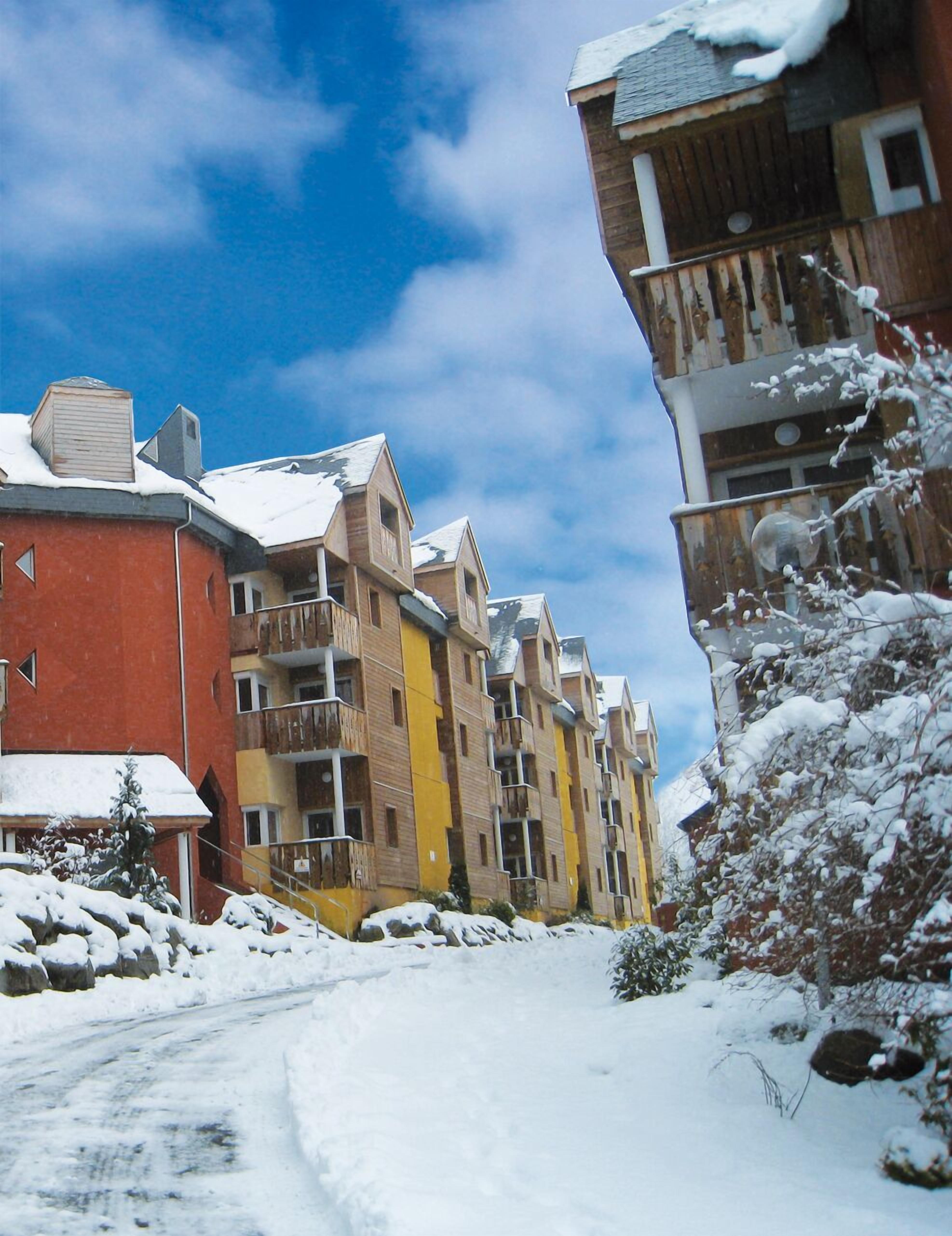 Una hilera de edificios de varios pisos con balcones, una carretera cubierta de nieve y un cielo azul despejado.