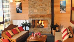 A cozy living room with a stone fireplace, wooden furniture, and a view of the outdoors. - Résidence Lagrange Vacances Domaine des 100 Lacs (Cauterets)