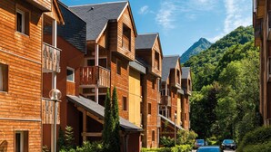 A row of wooden buildings with balconies, a mountain in the background, and a clear sky. - Résidence Lagrange Vacances Domaine des 100 Lacs (Cauterets)