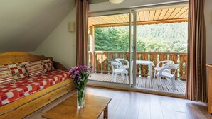 A cozy room with a wooden sofa, a small table, and a balcony with white chairs and a wooden table. - Résidence Lagrange Vacances Domaine des 100 Lacs (Cauterets)