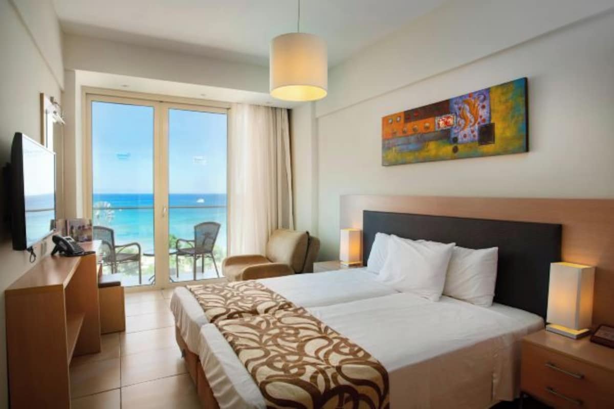 A hotel room with a bed, a desk, a chair, a TV, and a painting on the wall.