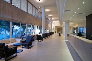 Un lobby amplio con mostrador de recepción, zona de estar con sofás y sillones, ventanas grandes que ofrecen vistas y un techo alto con iluminación empotrada.