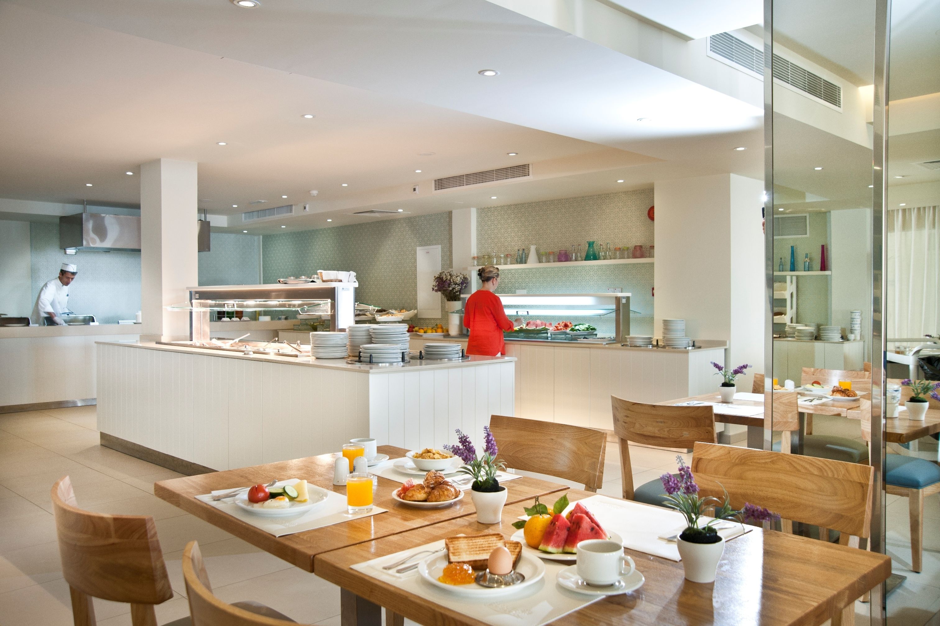 A modern hotel dining area with a central island, wooden tables, and a buffet counter.